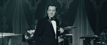 Movie still from “Beyond the Sea” (2004), directed by Kevin Spacey – A black and white photo of a man in a tuxedo holding a microphone; Medium shot, Over the shoulder angle