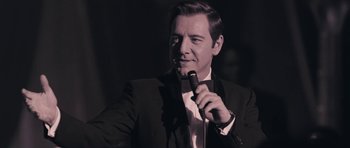 Movie still from “Beyond the Sea” (2004), directed by Kevin Spacey – A man holding a microphone in front of a crowd; Close Up shot, Over the shoulder angle