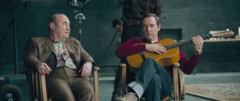 Movie still from “Beyond the Sea” (2004), directed by Kevin Spacey – A man sitting in a rocking chair with a guitar; Medium shot, High angle