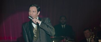 Movie still from “Beyond the Sea” (2004), directed by Kevin Spacey – A man in a suit and tie holding a microphone; Close Up shot, Over the shoulder angle