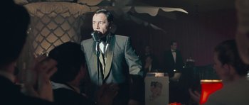 Movie still from “Beyond the Sea” (2004), directed by Kevin Spacey – A man in a suit and tie speaking into a microphone; Medium shot, Over the shoulder angle