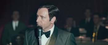Movie still from “Beyond the Sea” (2004), directed by Kevin Spacey – A man in a suit and bow tie is holding a microphone; Close Up shot, Over the shoulder angle