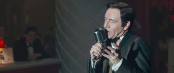 Movie still from “Beyond the Sea” (2004), directed by Kevin Spacey – A man in a suit and tie holding a microphone; Close Up shot, Over the shoulder angle