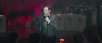 Movie still from “Beyond the Sea” (2004), directed by Kevin Spacey – A man in a suit and tie holding a microphone; Close Up shot, Over the shoulder angle