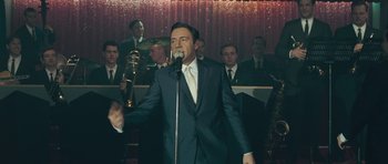 Movie still from “Beyond the Sea” (2004), directed by Kevin Spacey – A man in a suit and tie singing into a microphone in front of a group of men; Medium shot, Over the shoulder angle