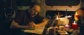 Movie still from “Beyond the Sea” (2004), directed by Kevin Spacey – A man sitting at a table writing on a sheet of paper next to a guitar; Close Up shot, High angle