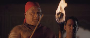 A man with a red hat holding a burning stick