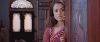 A beautiful woman in a red sari leaning against a wall