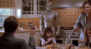 Movie still from “Bicentennial Man” (1999), directed by Chris Columbus – A person standing in a kitchen next to a person eating; Medium shot, Over the shoulder angle