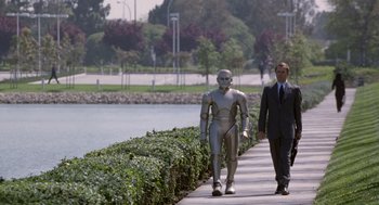 Movie still from “Bicentennial Man” (1999), directed by Chris Columbus – Two men walking down a sidewalk next to a body of water; Wide shot, High angle