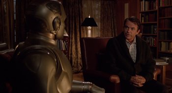 Movie still from “Bicentennial Man” (1999), directed by Chris Columbus – A man sitting in a chair next to a robot; Medium shot, Over the shoulder angle