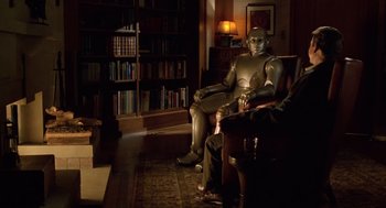 Movie still from “Bicentennial Man” (1999), directed by Chris Columbus – A man sitting in a chair next to a robot; Wide shot, Over the shoulder angle