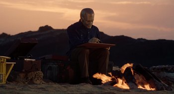 Movie still from “Bicentennial Man” (1999), directed by Chris Columbus – A man sitting on top of a suitcase next to a fire; Wide shot, Low angle