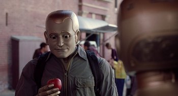 Movie still from “Bicentennial Man” (1999), directed by Chris Columbus – A man with a robot head holding an apple; Close Up shot, Over the shoulder angle