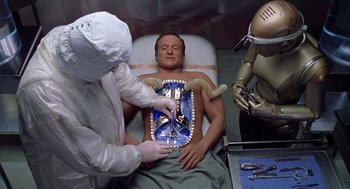 Movie still from “Bicentennial Man” (1999), directed by Chris Columbus – A man is being examined by a doctor and a robot; Medium shot, Overhead angle