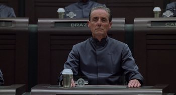 Movie still from “Bicentennial Man” (1999), directed by Chris Columbus – A man sitting at a table in front of a microphone; Medium shot, Low angle