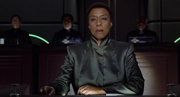 Movie still from “Bicentennial Man” (1999), directed by Chris Columbus – A woman sitting at a table in front of a group of people; Close Up shot, Low angle