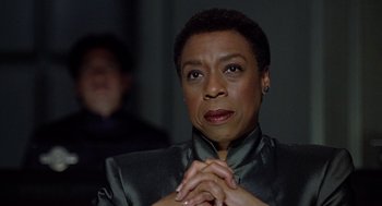 Movie still from “Bicentennial Man” (1999), directed by Chris Columbus – An older woman with short black hair wearing a black jacket; Close Up shot, Over the shoulder angle