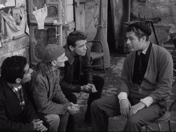 Movie still from “Big Deal on Madonna Street” (1958), directed by Mario Monicelli – A group of men sitting on the ground talking to each other; Medium shot, Over the shoulder angle