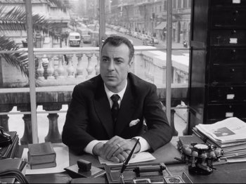 Movie still from “Big Deal on Madonna Street” (1958), directed by Mario Monicelli – A man sitting at a desk in front of a window; Medium shot, Low angle