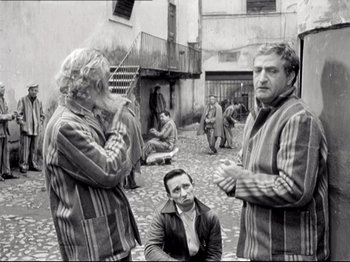 Movie still from “Big Deal on Madonna Street” (1958), directed by Mario Monicelli – A group of people standing around in a courtyard; Medium shot, Over the shoulder angle