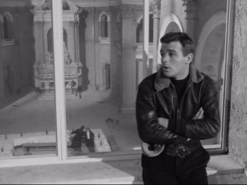 Movie still from “Big Deal on Madonna Street” (1958), directed by Mario Monicelli – A man in a leather jacket standing with his arms crossed; Medium shot, Low angle