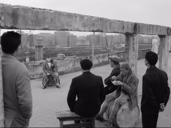 Movie still from “Big Deal on Madonna Street” (1958), directed by Mario Monicelli – A black and white photo of a group of people sitting on a bench; Wide shot, Over the shoulder angle