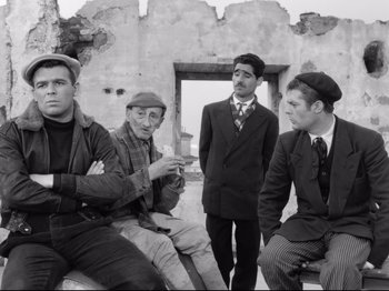Movie still from “Big Deal on Madonna Street” (1958), directed by Mario Monicelli – A group of men sitting next to each other in front of a building; Medium shot, Low angle