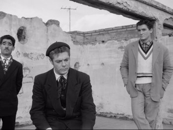 Movie still from “Big Deal on Madonna Street” (1958), directed by Mario Monicelli – Two young men in suits and hats sitting on the side of the street; Medium shot, Low angle