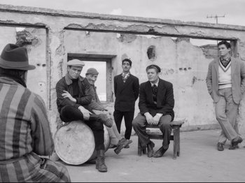 Movie still from “Big Deal on Madonna Street” (1958), directed by Mario Monicelli – A black and white photo of a group of men sitting and standing; Wide shot, Low angle