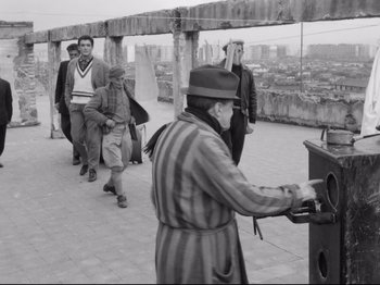 Movie still from “Big Deal on Madonna Street” (1958), directed by Mario Monicelli – An older man in a striped shirt and a hat is near a group of people; Wide shot, Low angle