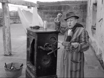 Movie still from “Big Deal on Madonna Street” (1958), directed by Mario Monicelli – An old man in a striped bathrobe and a hat is standing next to an oven; Medium shot, High angle