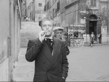 Movie still from “Big Deal on Madonna Street” (1958), directed by Mario Monicelli – A man smoking a cigarette while standing next to another man; Medium shot, Low angle