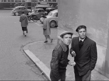 Movie still from “Big Deal on Madonna Street” (1958), directed by Mario Monicelli – A couple of men standing next to each other on a sidewalk; Medium shot, High angle