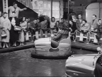 Movie still from “Big Deal on Madonna Street” (1958), directed by Mario Monicelli – A man riding on the back of a bumper car at an amusement park; Wide shot, High angle