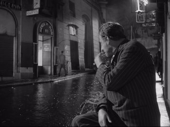 Movie still from “Big Deal on Madonna Street” (1958), directed by Mario Monicelli – A black and white photo of a man sitting on a bench in the rain; Wide shot, High angle