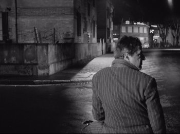 Movie still from “Big Deal on Madonna Street” (1958), directed by Mario Monicelli – A man riding a bike down a street at night; Wide shot, Over the shoulder angle