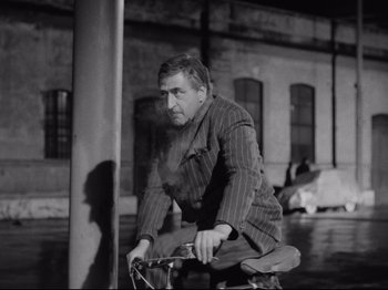 Movie still from “Big Deal on Madonna Street” (1958), directed by Mario Monicelli – A black and white photo of a man riding a bike; Medium shot, Low angle