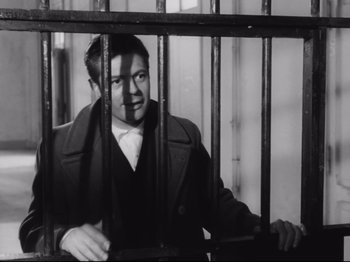 Movie still from “Big Deal on Madonna Street” (1958), directed by Mario Monicelli – A black and white photo of a man behind bars; Medium shot, Low angle