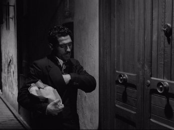 Movie still from “Big Deal on Madonna Street” (1958), directed by Mario Monicelli – A black and white photo of a man in a suit holding a bag; Medium shot, Low angle