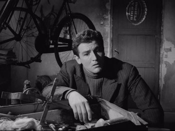 Movie still from “Big Deal on Madonna Street” (1958), directed by Mario Monicelli – A black and white photo of a man sitting in front of a bicycle; Medium shot, Low angle