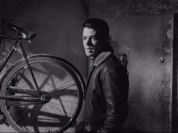 Movie still from “Big Deal on Madonna Street” (1958), directed by Mario Monicelli – A man standing next to a bicycle in a room; Medium shot, High angle