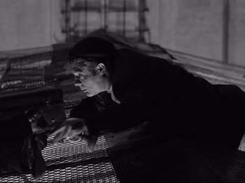 Movie still from “Big Deal on Madonna Street” (1958), directed by Mario Monicelli – A man leaning on a metal fence looking at a laptop; Medium shot, Low angle