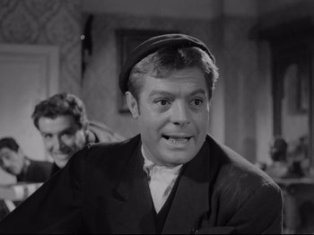 Movie still from “Big Deal on Madonna Street” (1958), directed by Mario Monicelli – A man in a suit and a hat is smiling for the camera; Close Up shot, Over the shoulder angle