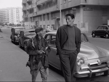 Movie still from “Big Deal on Madonna Street” (1958), directed by Mario Monicelli – Two men are walking down the street near a parked car; Wide shot, Low angle