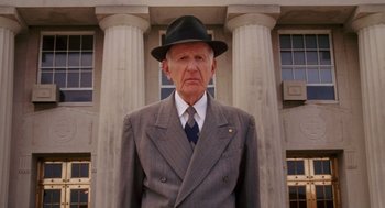 Movie still from “Big Fish” (2003), directed by Tim Burton – An older man in a suit and hat stands in front of a building; Medium shot, Low angle