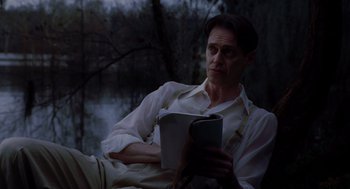 Movie still from “Big Fish” (2003), directed by Tim Burton – A man sitting on the ground reading a book; Medium shot, Low angle