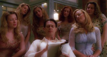 Movie still from “Big Fish” (2003), directed by Tim Burton – A man sitting in front of a group of women; Medium shot, Low angle