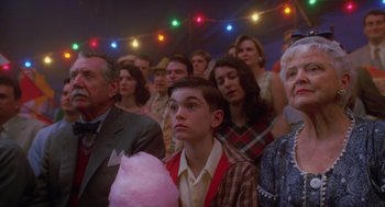 Movie still from “Big Fish” (2003), directed by Tim Burton – A group of people sitting in a room with lights in the background; Medium shot, High angle