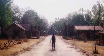 Movie still from “Big Fish” (2003), directed by Tim Burton – A man walking down a dirt road in an abandoned town; Extreme Wide shot, Low angle